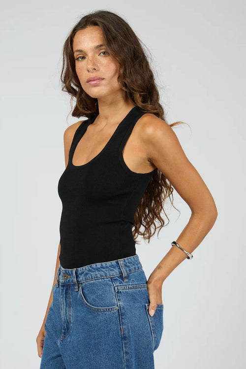 Woman wearing a black tank top and blue jeans against a plain background