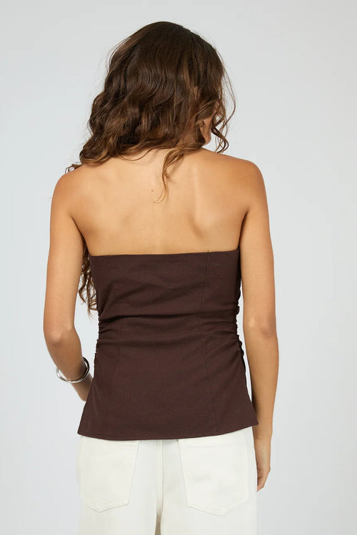 Woman wearing a brown strapless top and white pants on a plain background