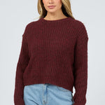Woman wearing a burgundy sweater and light blue jeans on a white background