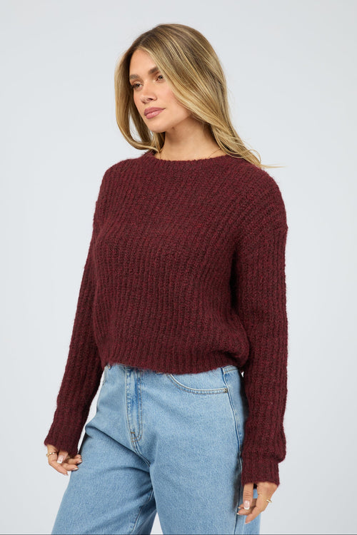 Woman wearing a burgundy sweater and light blue jeans on a plain background
