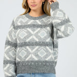 Woman wearing a gray and white patterned sweater with blue jeans on a light gray background