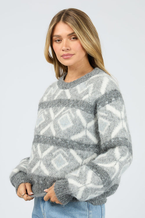 Woman wearing a gray and white patterned sweater on a plain background