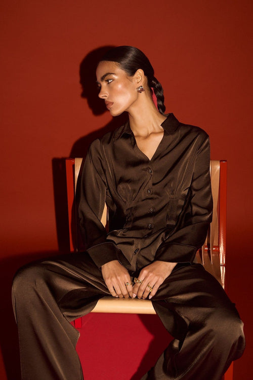 Person wearing a black outfit sitting on a chair against a red background
