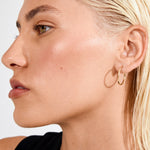 Close-up of a person with blonde hair and hoop earrings on a plain background