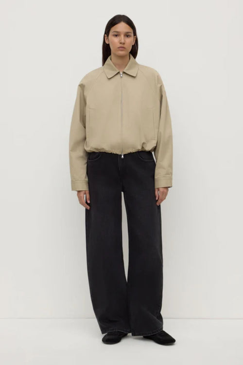 Person wearing a beige jacket and black pants on a white background