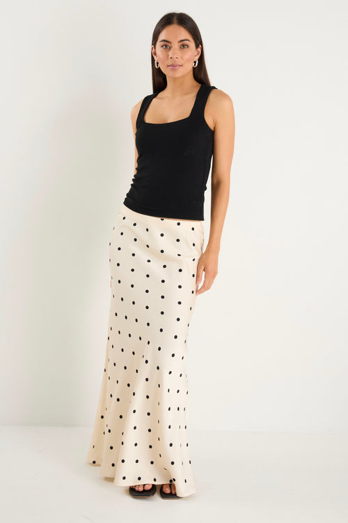 the model wears a cream maxi skirt with black polka dots and a black tank top