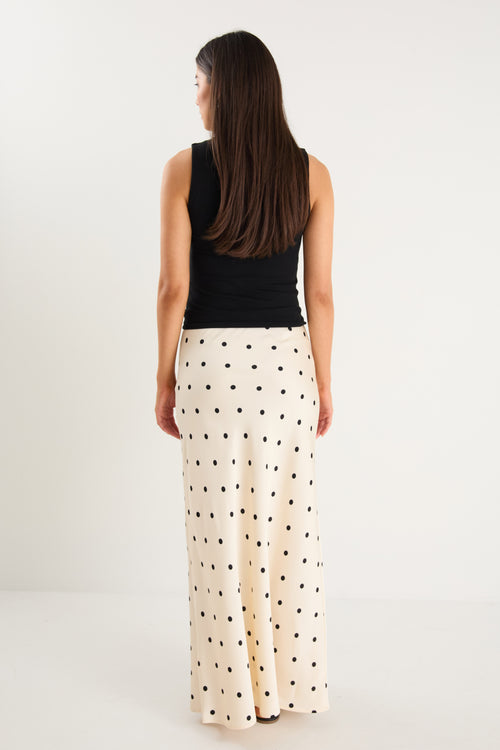 the model wears a cream maxi skirt with black polka dots and a black tank top