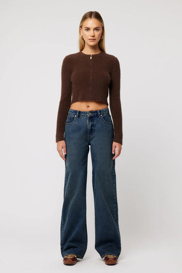 Model wears a baggy dark low rise jean with a brown long sleeve top