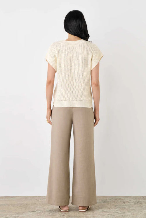 Woman wearing a beige top and wide-leg pants against a white background