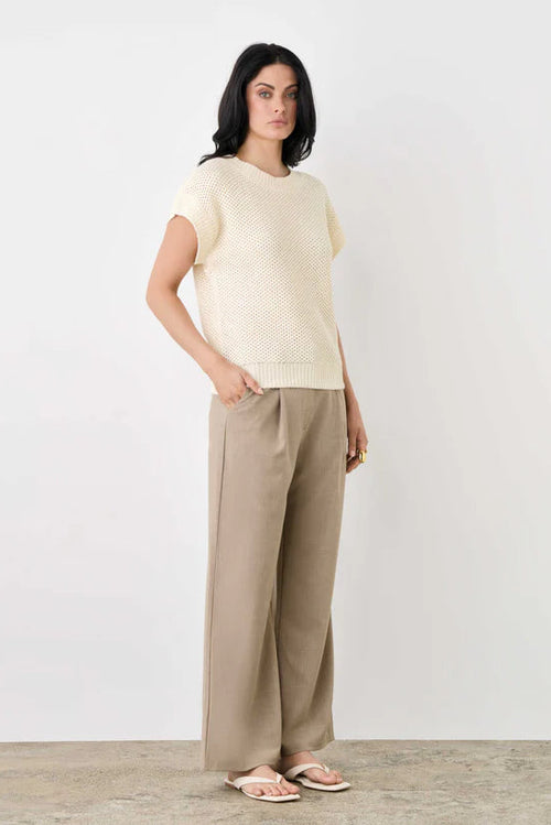 Woman wearing a light-colored top and beige pants on a white background