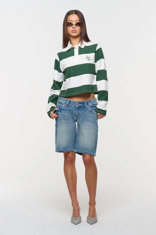 Woman wearing a green and white striped shirt with denim shorts on a white background