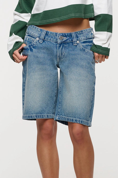 A person wearing light-wash blue denim shorts with a green and white striped long-sleeve top, shown from the chest to mid-thigh against a plain light background.