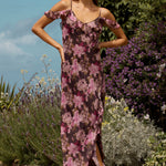 Woman in a floral dress standing in a garden with flowers and plants around her.