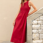 Woman in a red dress standing on a stone staircase against a beige wall.
