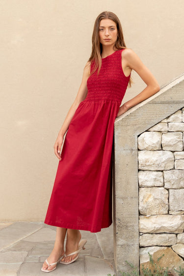 Woman in a red dress standing on a stone staircase against a beige wall.