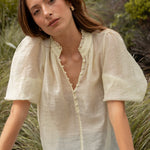 Woman sitting outdoors in a natural setting wearing a light blouse and jeans.