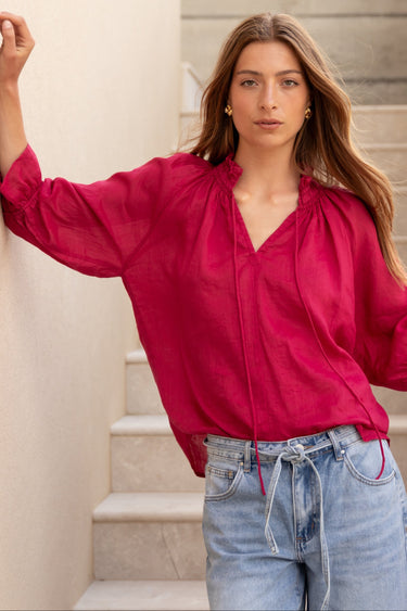 Woman wearing a red blouse and blue jeans standing on stone steps.