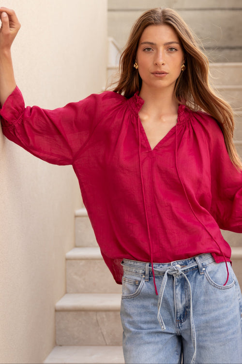 Woman wearing a red blouse and blue jeans standing on stone steps.