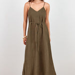 A woman modeling a long olive green spaghetti-strap maxi dress with a tie waist, standing against a plain white studio background.