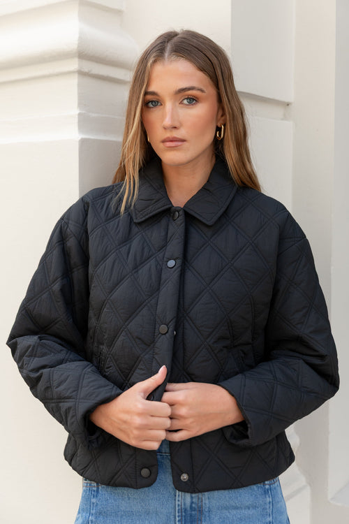 Woman wearing a black quilted jacket against a white wall