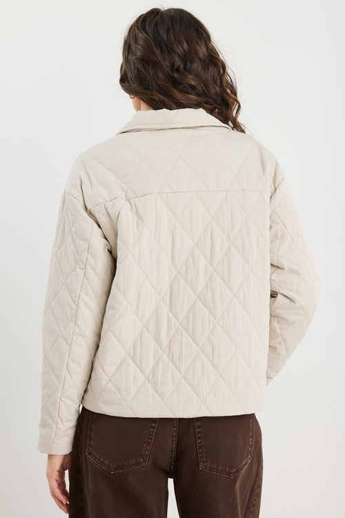 Person wearing a beige quilted jacket on a white background
