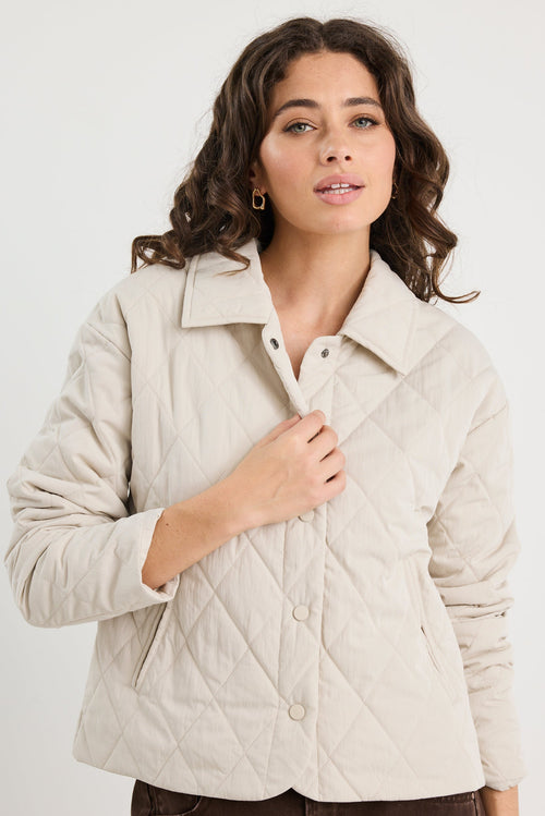 Woman wearing a beige quilted jacket against a white background