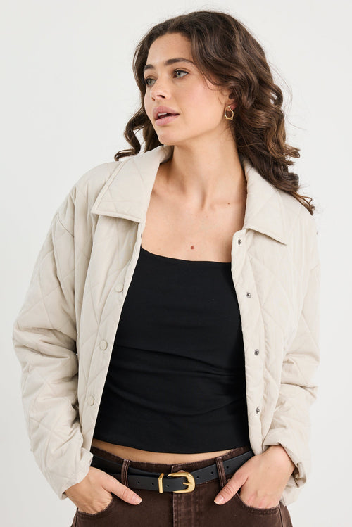 Woman wearing a beige jacket, black top, and brown pants on a white background