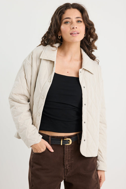 Woman wearing a beige jacket over a black top and brown pants on a white background