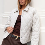 Woman wearing a white quilted jacket against a white wall