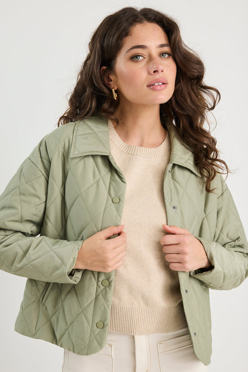 Woman wearing a green quilted jacket over a beige sweater on a white background