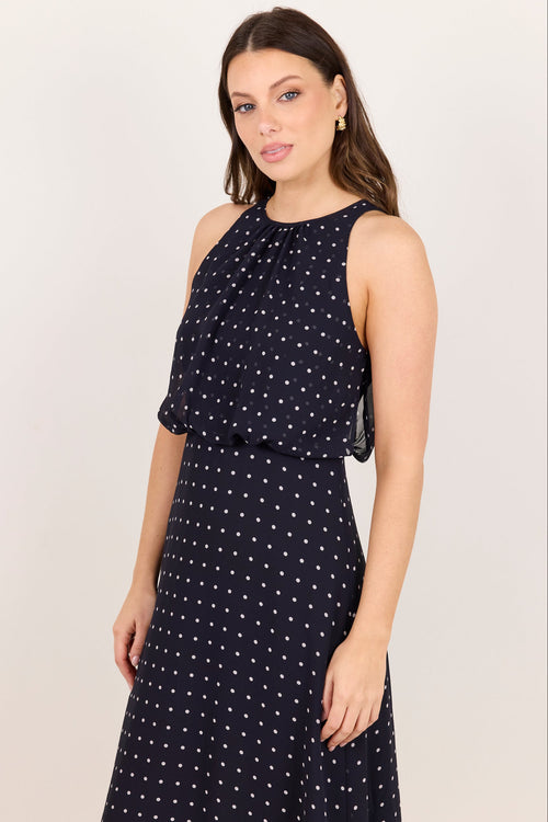 A woman modeling a sleeveless navy blue dress with a white polka dot pattern against a plain light background.