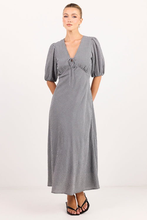 A woman modeling a gray midi-length dress with short puff sleeves, a deep V-neckline, and a gathered waist detail, paired with black sandals against a plain white studio background.