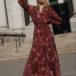 Woman in a red floral dress waving in front of a classical building.