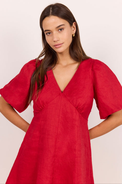 A woman modeling a vibrant red dress with short puff sleeves, a deep V-neckline, and a gathered waist, set against a plain light background.
