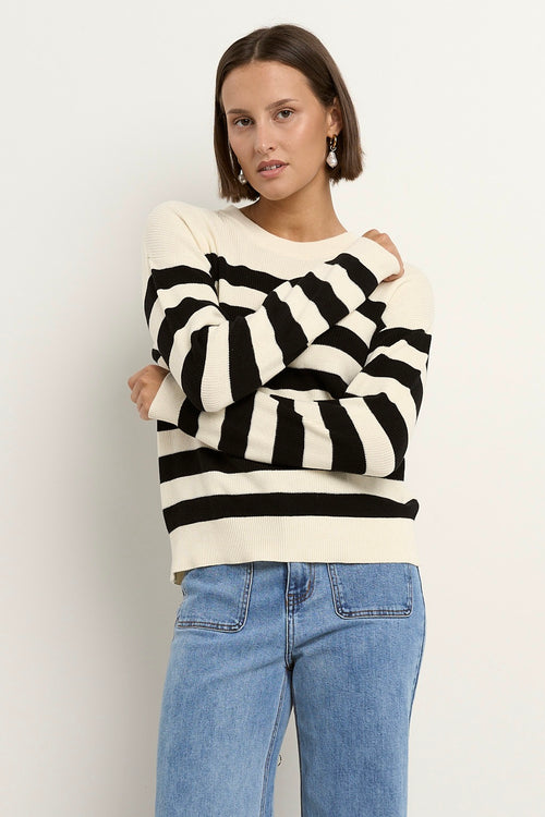 Woman wearing a black and ivory striped crew neck sweater with full-length sleeves, styled casually with light blue wide-leg jeans.