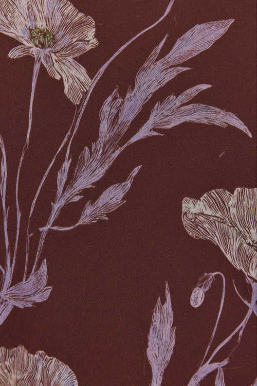 A close-up of a floral patterned surface with muted lavender botanical stems and flowers on a dark brown background.