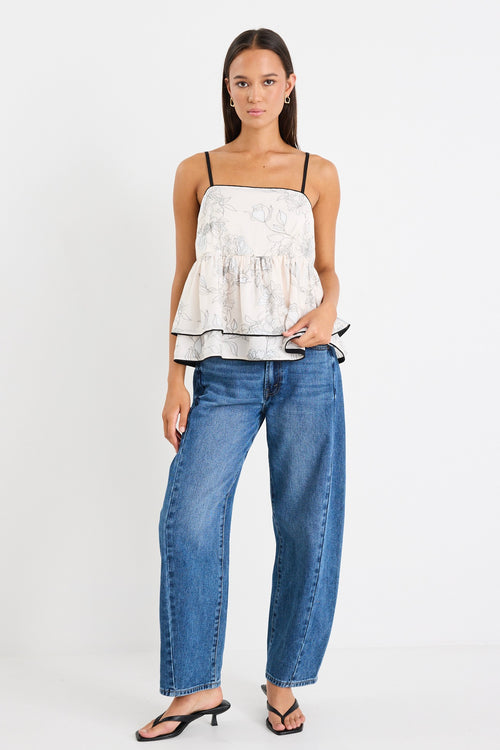 model wears a white floral tank top with blue jeans