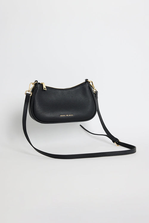 Black pebble-textured leather shoulder bag with gold hardware, featuring a curved silhouette, double adjustable straps and top zip closure. Stylish small black handbag from Among the Brave, ideal for everyday wear.