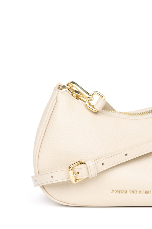 A close-up of a cream-colored pebbled leather shoulder bag with gold-tone hardware and a matching strap,