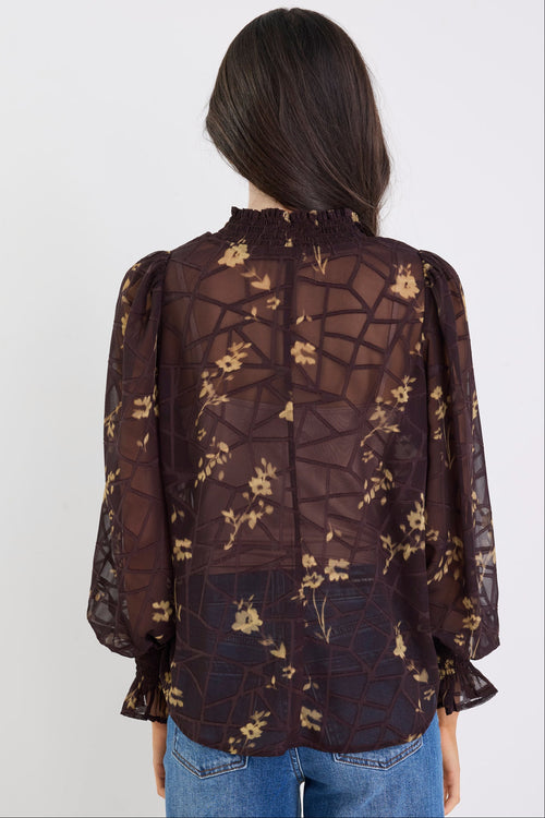 Person wearing a sheer floral blouse with long sleeves and blue jeans on a white background