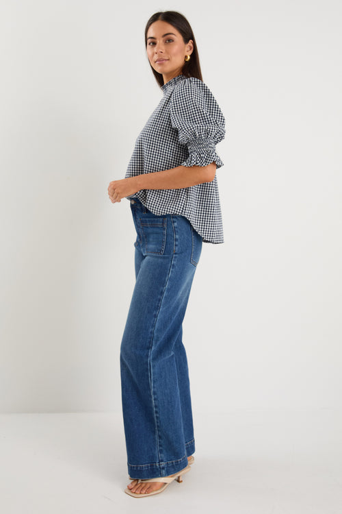 model wearing gingham shirred top and blue jeans. 