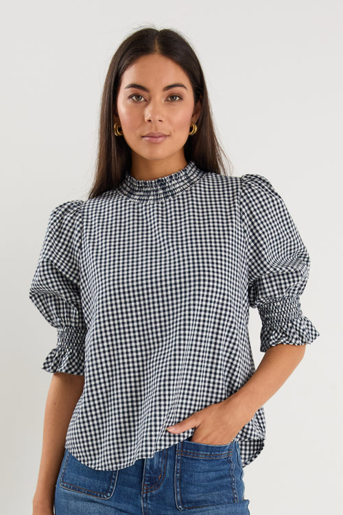 model wearing gingham shirred top and blue jeans. 