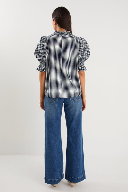 model wearing gingham shirred top and blue jeans. 