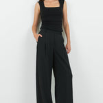 Woman wearing a black sleeveless top and wide-leg pants on a white background