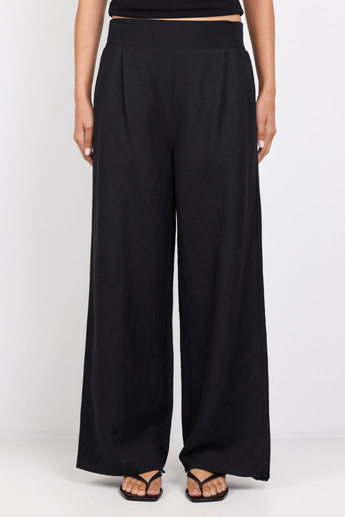 Person wearing black high-waisted pants and a black top on a white background