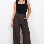 Woman wearing a black sleeveless top and brown wide-leg pants on a white background