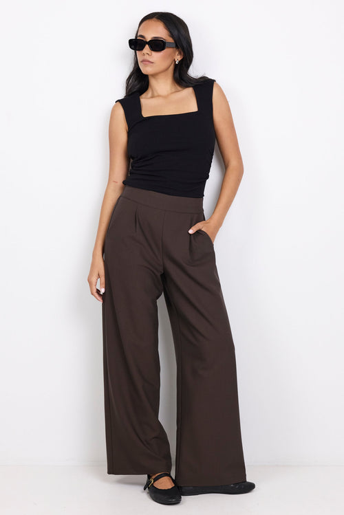Woman wearing a black sleeveless top and brown wide-leg pants on a white background