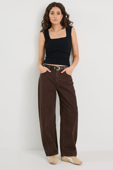 Woman wearing a black tank top and brown pants on a white background