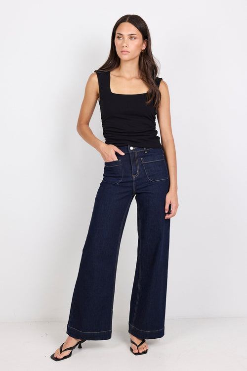 Woman wearing dark blue jeans and a black top on a white background