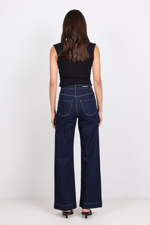 Woman wearing dark blue jeans and a black top on a white background